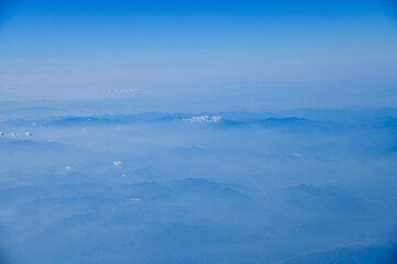 Fototapeta premium The view of the stunning landscape with mountains and clouds from the airplane window. Aerial view of the natural scene, mountain range. Travel and landscape scene. Travel and nature concept. 