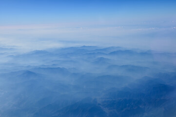 The view of the stunning landscape with mountains and clouds from the airplane window. Aerial view of the natural scene, mountain range. Travel and landscape scene. Travel and nature concept. 