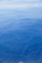Fototapeta premium The view of the stunning landscape with mountains and clouds from the airplane window. Aerial view of the natural scene, mountain range. Travel and landscape scene. Travel and nature concept. 