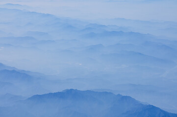 The view of the stunning landscape with mountains and clouds from the airplane window. Aerial view of the natural scene, mountain range. Travel and landscape scene. Travel and nature concept. 