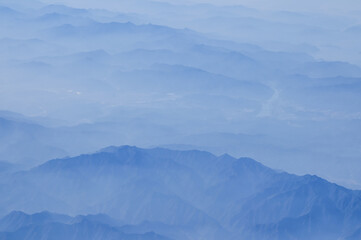 The view of the stunning landscape with mountains and clouds from the airplane window. Aerial view of the natural scene, mountain range. Travel and landscape scene. Travel and nature concept. 