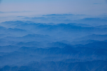 Fototapeta premium The view of the stunning landscape with mountains and clouds from the airplane window. Aerial view of the natural scene, mountain range. Travel and landscape scene. Travel and nature concept. 