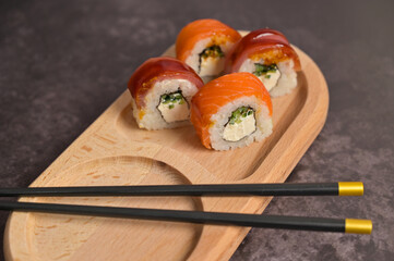 Set of sushi roll with rice and fish and chopsticks on wooden serving board. Dark black texture background with copy space. Close up. Japan menu. Asian food