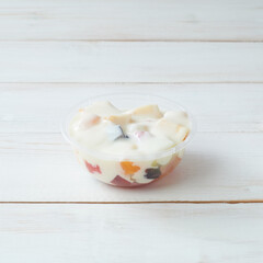 Fresh Fruit Salad in a Clear Plastic Bowl Garnished With Creamy Dressing on a Wooden Table