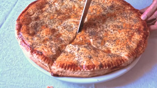 Close-up of a freshly baked puff pastry savoury pie decorated with poppy seeds, which is cut in half with a knife.