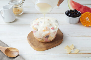 Fresh Fruit Salad in a Plastic Bowl With Creamy Dressing and Assorted Fruits on a Wooden Table