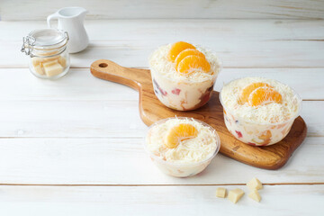 Fruit Salad in a Plastic Bowl Garnished With Orange Slices and Shredded Coconut, salad dressing and grated cheese Displayed on a Wooden Cutting Board