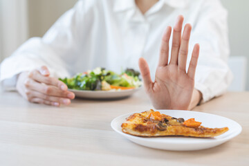 Diet concept, asian young woman close up hand push out away Pizza, refuse junk process, carb food on plate, choose green vegetable salad, eat low fat for good health. Female people getting weight loss