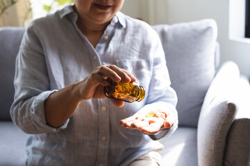 Dietary supplement health care concept, asian senior woman hand holding fish oil pills, drug medical tablet pouring capsules from medication bottle, aged take vitamin for treatment body strong at home