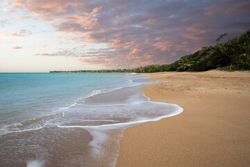 Deserted wide sandy beach with turquoise blue sea. Tropical plants of a bay at sunset in the...