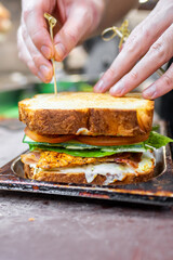 A close-up of a hand assembling a sandwich with layers of lettuce, delicious fillings, and toasted bread. A toothpick holds the sandwich together, highlighting fresh ingredients.