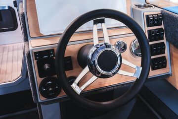 The steering wheel of a boat is made of wood and black leather. The steering wheel is in the center...