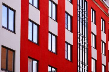 A modern apartment building with numerous windows and a red and white exterior.