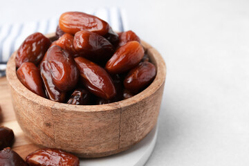 Tasty dried dates in wooden bowl on white table, closeup. Space for text