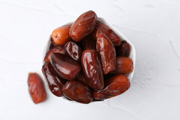 Tasty sweet dried dates in paper bag on white table, top view