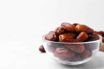 Tasty dried dates in glass bowl on white table, closeup. Space for text