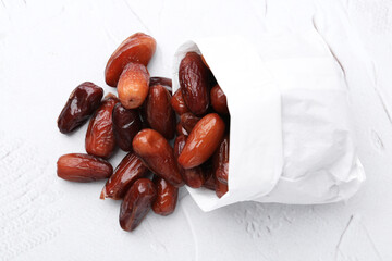 Tasty sweet dried dates in paper bag on white table, top view