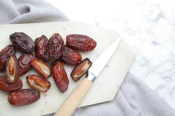 Many tasty dried dates, cutting board and knife on white marble table, top view