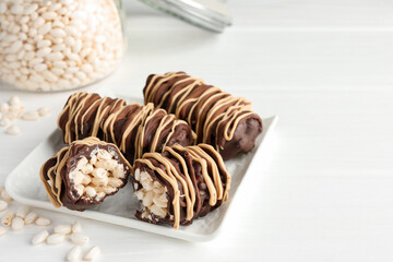 Delicious chocolate puffed rice bars on white wooden table, closeup. Space for text