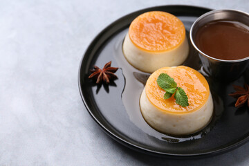 Tasty puddings with caramel sauce served on light grey table, closeup. Space for text