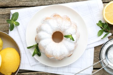 Tasty lemon cake with powdered sugar, fresh fruits and mint on wooden table, flat lay