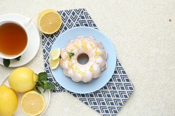 Delicious cake with lemon zest, powdered sugar, mint, tea and citrus fruits on light textured table, flat lay. Space for text