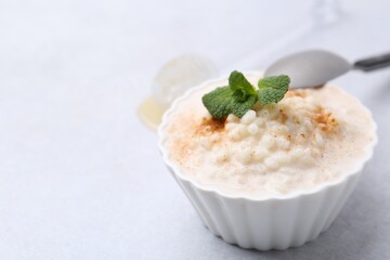 Tasty rice pudding with cinnamon and mint on light grey table, closeup. Space for text