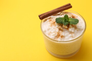 Tasty rice pudding with cinnamon, mint and nuts in glass bowl on yellow background, closeup. Space for text