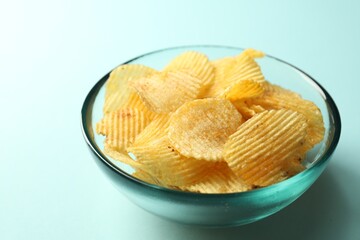 Tasty potato chips on light blue background, closeup