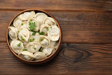Delicious dumplings with fresh green onion and parsley on wooden table, top view. Space for text