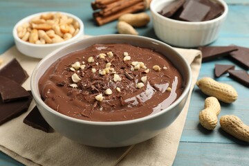 Tasty chocolate pudding in bowl and ingredients on light blue wooden table, closeup
