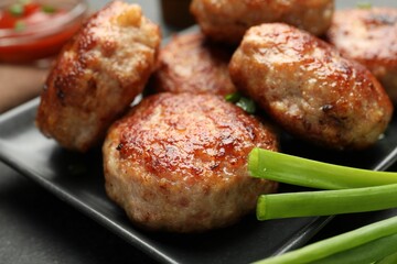 Delicious patties with green onions on black table, closeup