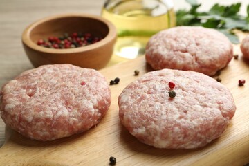 Many uncooked patties and spices on wooden table, closeup