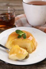 Delicious pudding with caramel sauce and mint served on wooden table, closeup