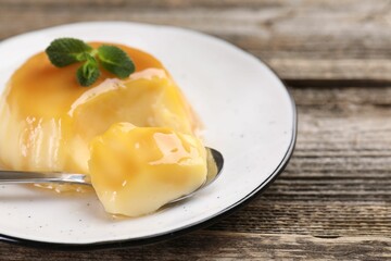 Delicious pudding with caramel sauce and mint served on wooden table, closeup