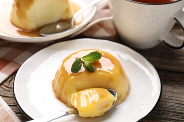 Delicious pudding with caramel sauce and mint served on wooden table, closeup