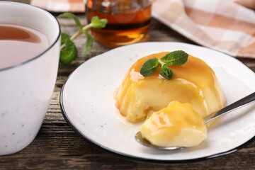 Delicious pudding with caramel sauce and mint served on wooden table, closeup