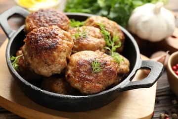 Tasty patties and dill in frying pan on wooden table, closeup