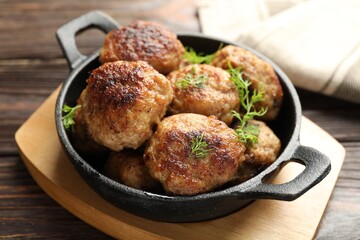 Tasty patties and dill in frying pan on wooden table, closeup