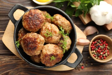 Tasty patties, dill in frying pan and peppercorns on wooden table, flat lay