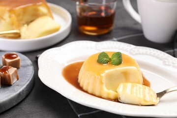 Delicious pudding with caramel sauce and mint served on gray table, closeup