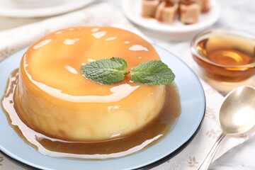 Delicious pudding with caramel sauce and mint on white table, closeup