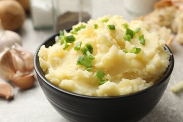 Delicious mashed potato with green onions in bowl on grey table, closeup