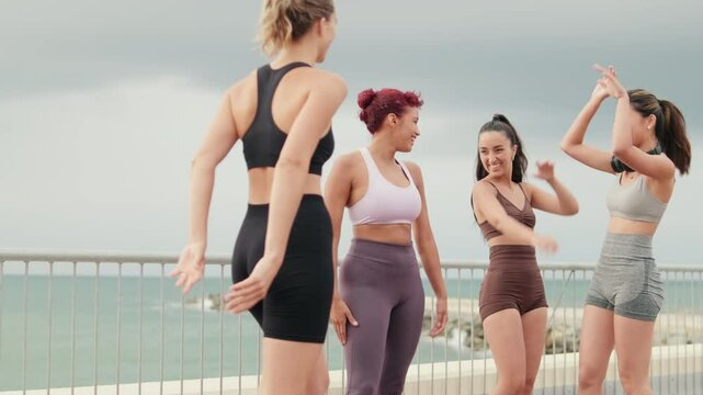 Four diverse female friends celebrate their fitness workout with joyful high fives by the beach.  They enjoy their active lifestyle together.