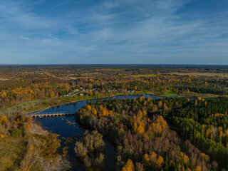 Naklejka premium Aerial photo of beautiful autumn landscape. Jagala (Estonian Jägala) river meandering through a dense forest of mixed trees - in gold, orange and green colors. Small bridge crosses the river. 