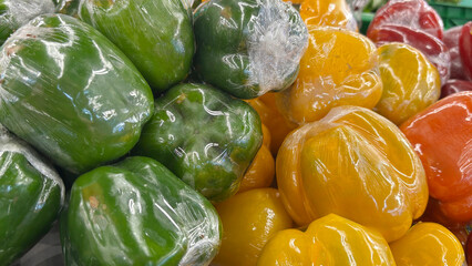 Fresh Green, Yellow, and Red Bell Peppers in Plastic Wrap Displayed at a Market on a Bright Sunny Day