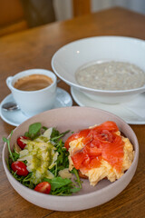 Delicious healthy breakfast spread featuring creamy oat porridge, scrambled eggs topped with smoked salmon, a fresh arugula salad with cherry tomatoes and parmesan, paired with a smooth café crema. 