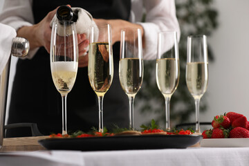 Waiter filling glasses with champagne indoors, closeup