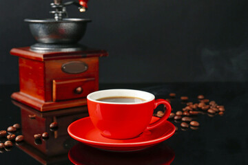 Red cup with coffee, vintage grinder and roasted beans on black background