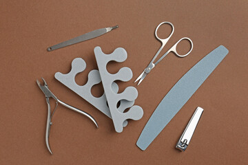 Set of pedicure tools on brown background, flat lay